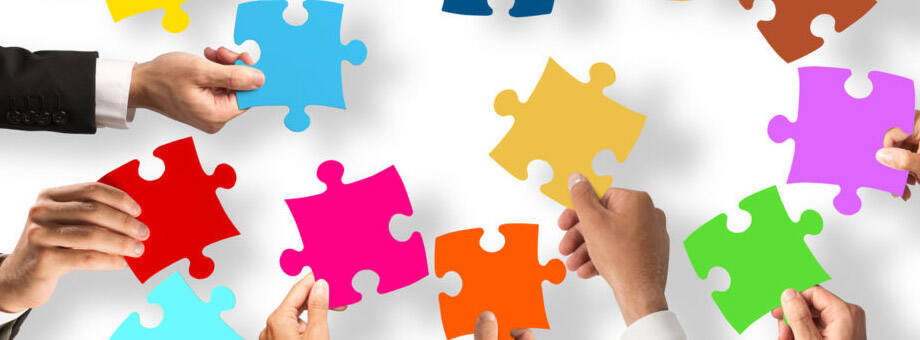 Pezzi di puzzle colorati su sfondo bianco tenuti dalle mani di alcune persone