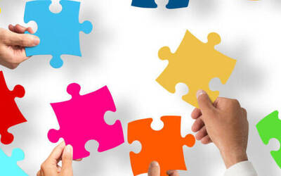 Pezzi di puzzle colorati su sfondo bianco tenuti dalle mani di alcune persone