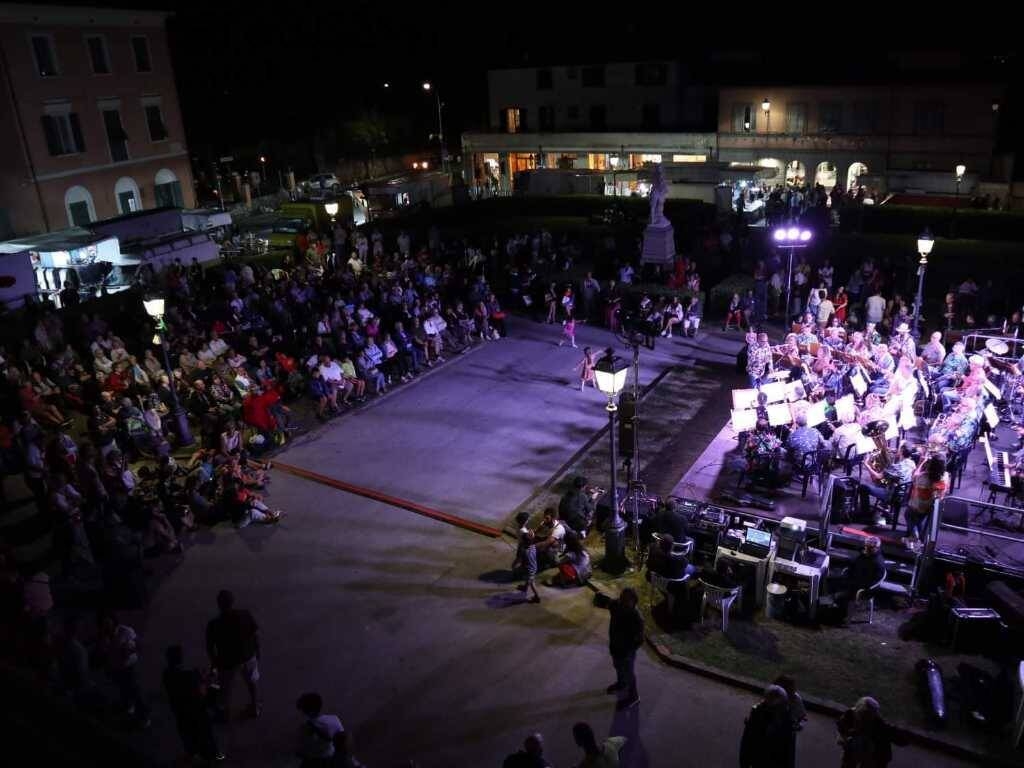 Veduta di Piazza Garibaldi a Calci durante un evento notturno con orchestra sul palco e il pubblico seduto di fronte