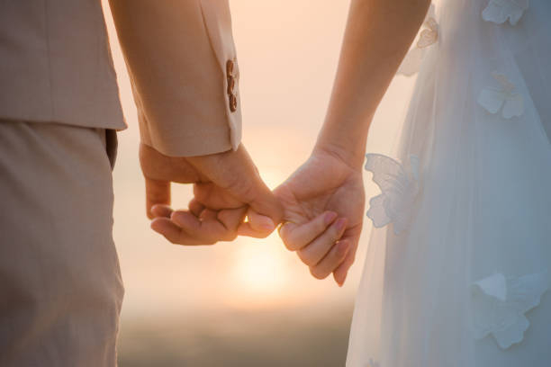 Dettaglio delle mani di una sposa e uno sposo che si intrecciano alla luce del tramonto