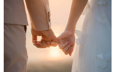 Dettaglio delle mani di una sposa e uno sposo che si intrecciano alla luce del tramonto