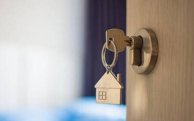 Una chiave, con portachiavi a forma di casa, inserita nella serratura di una porta semiaperta